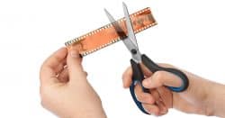 Hand holding a piece of film with the other hand using scissors to cut it.