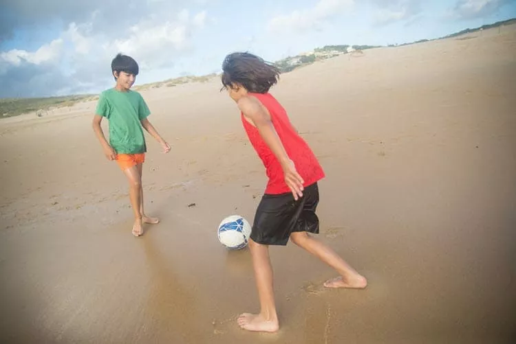 Dutch angle shot of boys on a beach playing football.