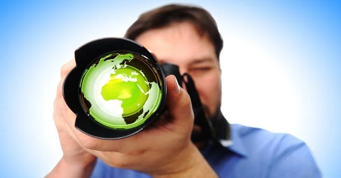 Videographer aiming a large lens camera at the viewer depicting shooting video.